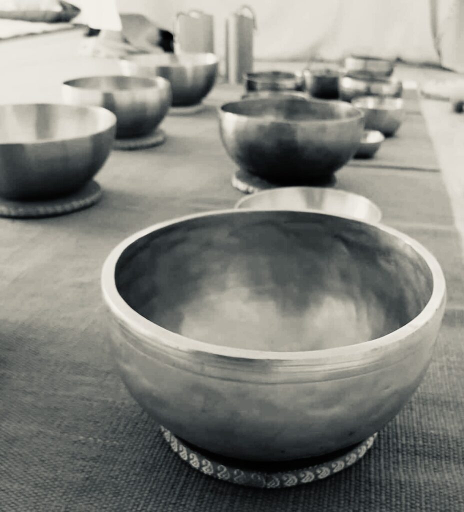Zbliżenie kilku metalowych mis śpiewających ułożonych na macie, z naciskiem na misę na pierwszym planie. Obraz jest czarno-biały, tworząc spokojną i pogodną atmosferę.