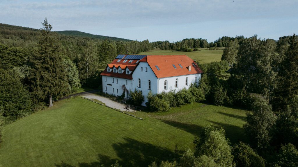 Biały dom z czerwonym dachem otoczony drzewami.