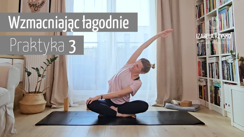 Kobieta w jasnoróżowej koszuli i czarnych legginsach siedzi ze skrzyżowanymi nogami na macie do jogi, wyciągając rękę w bok. Tekst w języku polskim brzmi: Wzmacniając łagodną Praktykę 3. Znajduje się w przytulnym, oświetlonym słońcem pokoju z półkami na książki i roślinami.