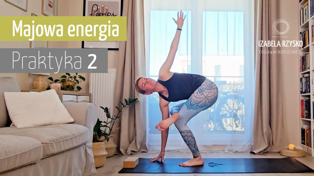 Iza Rzysko ćwiczy jogę online w jasnym salonie, wykonując skręcającą pozę na macie. Tekst brzmi "Majowa energia Praktyka 2" i "Izabela Rzysko Joga & Mindfulness". Światło słoneczne wpada przez duże okna.
